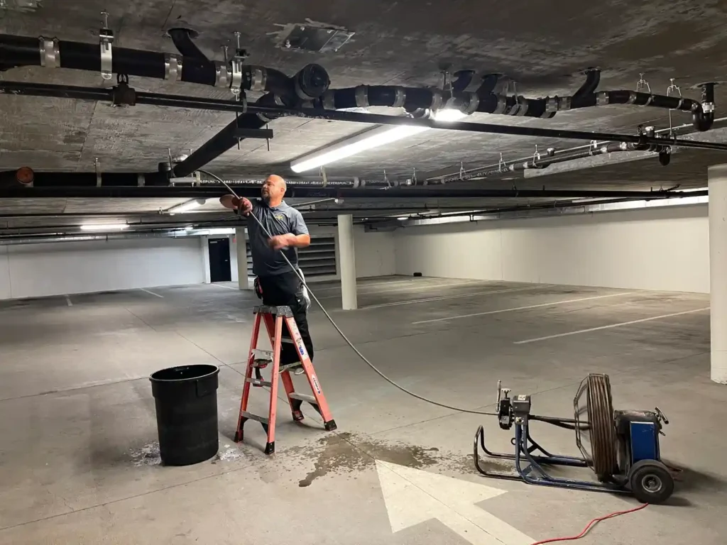 Handy Bay Plumbing technician servicing overhead pipes in a commercial parking structure in Redwood City CA